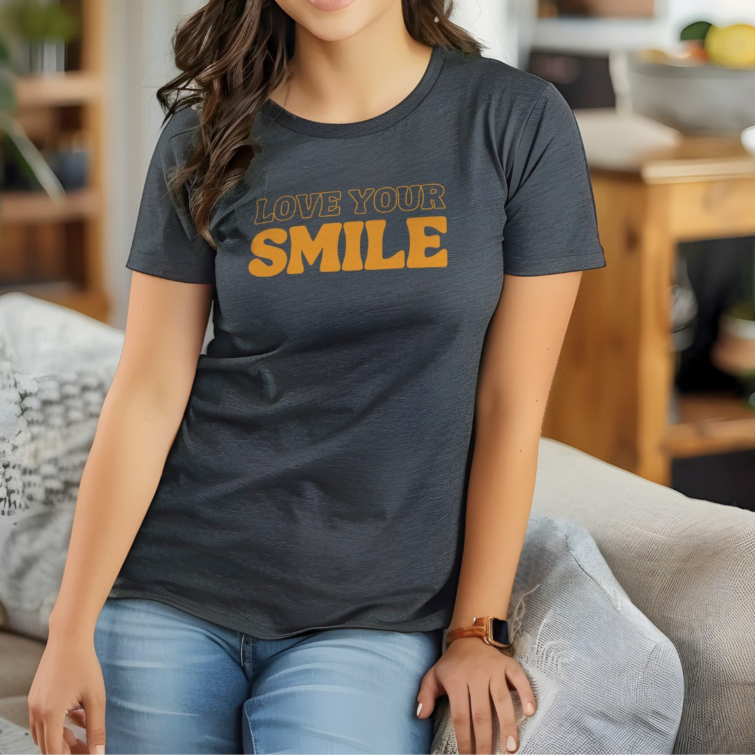 Woman wearing a dark gray t-shirt with 'LOVE YOUR SMILE' text in orange, sitting on a couch.